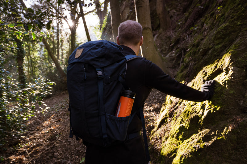 Carregar imagem no visualizador da galeria, Hiker climbing a steep forest path with an orange LifeSaver Liberty in his backpack