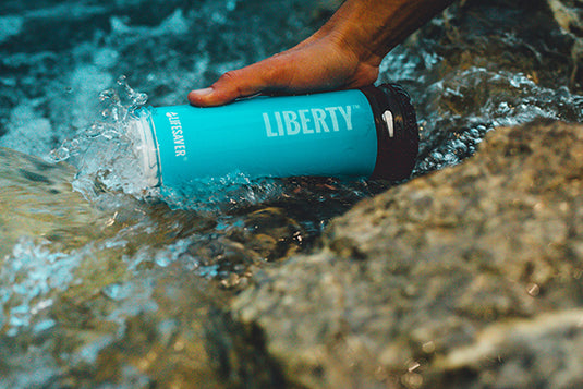 A blue LifeSaver Liberty bottle collecting water from a stream