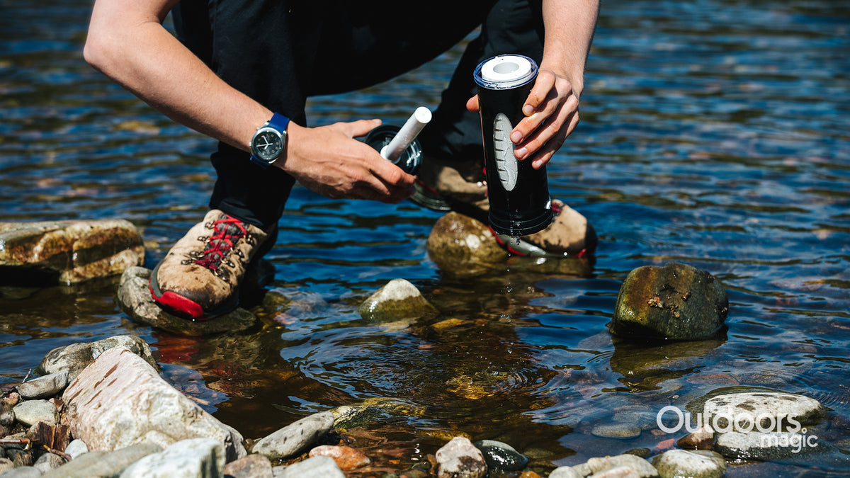 Person cleaning a LifeSaver Liberty by a stream with 'Outdoors Magic' branding.